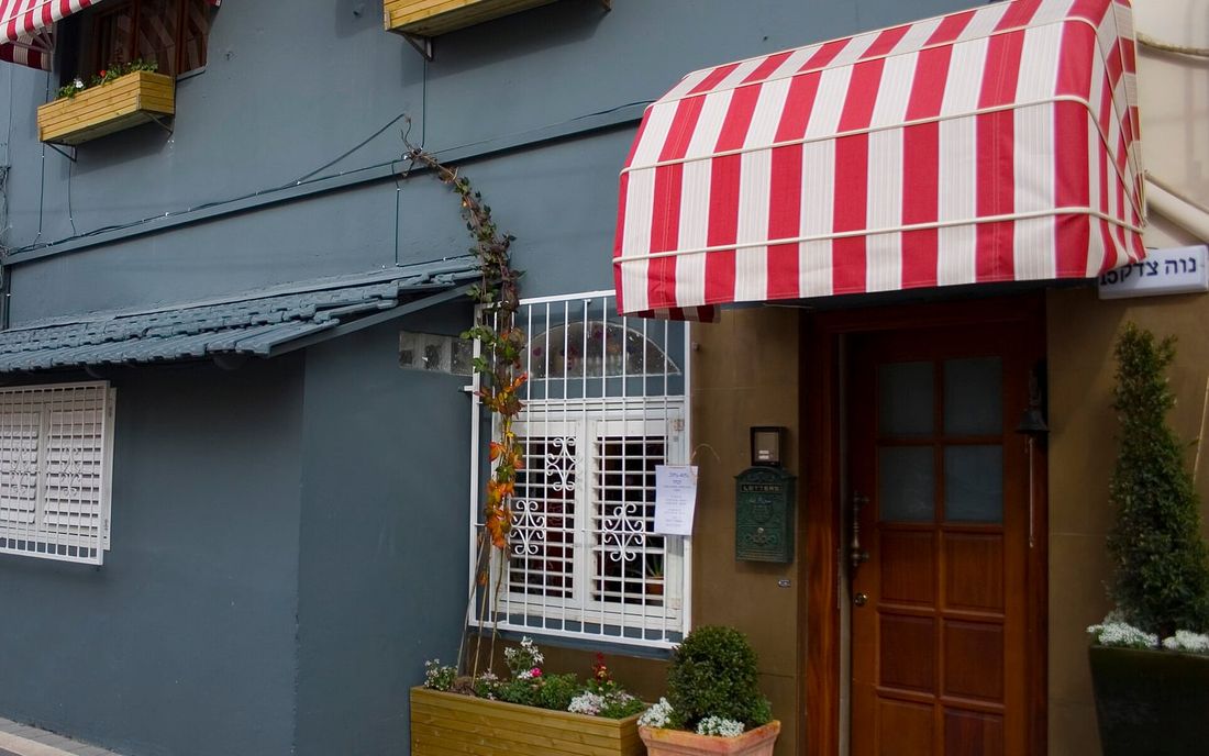 Toldo capota de lona listrada vermelha e branca sobre uma porta de madeira, com floreiras na fachada