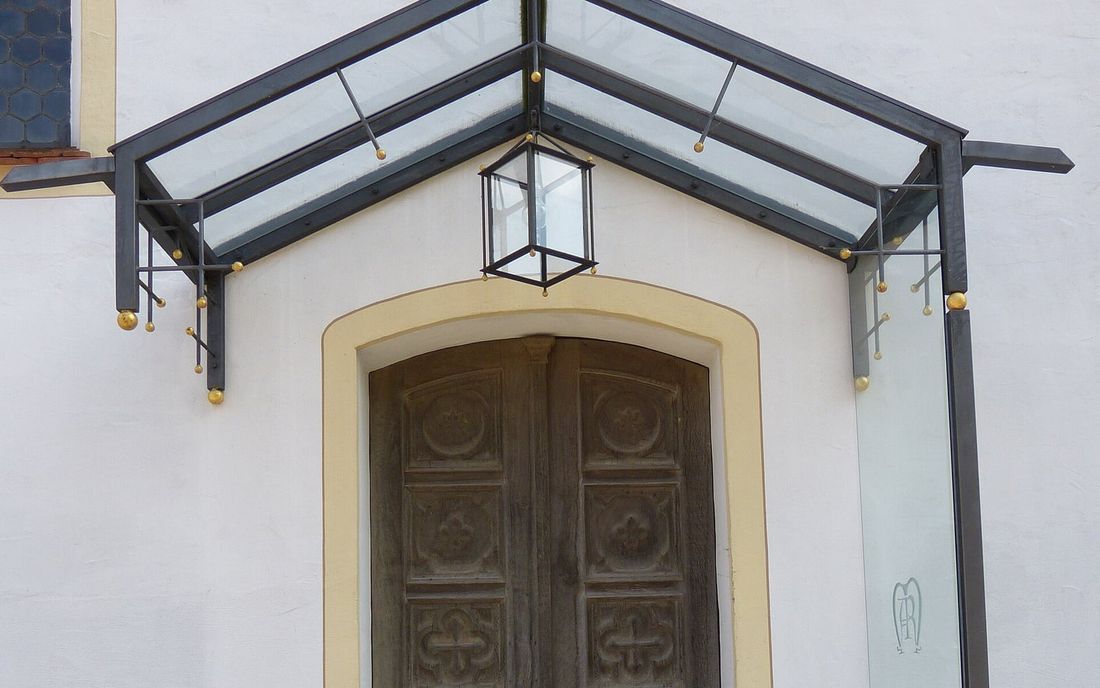 Toldo transparente com estrutura metálica escura e luminária, sobre uma porta de madeira